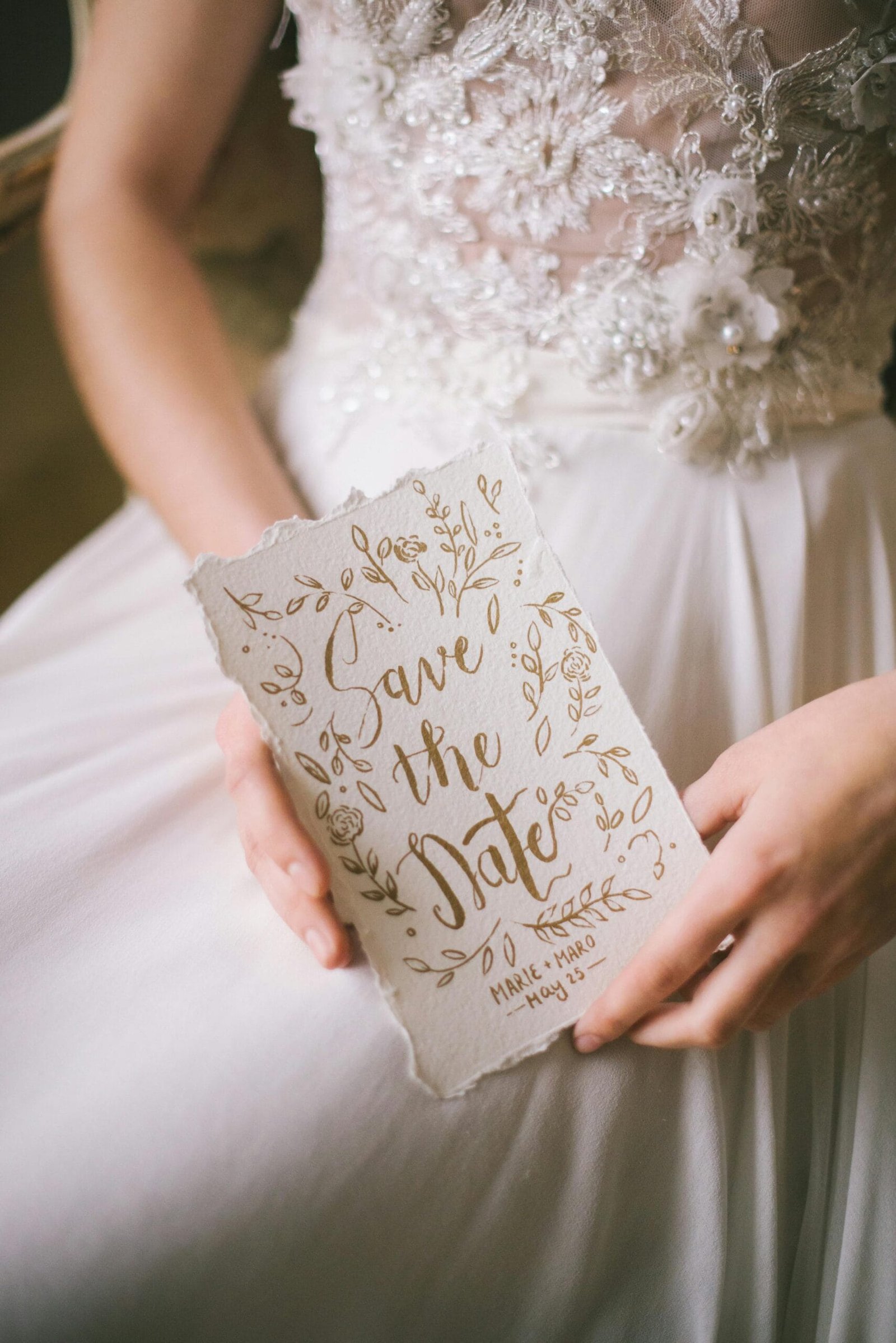 Wedding Websites. A close-up of a bride holding an elegant 'Save the Date' card with intricate calligraphy.