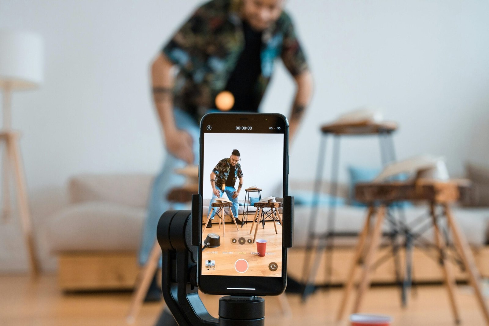 "Content Creation" Man recording video content with smartphone on a tripod in a cozy living room.